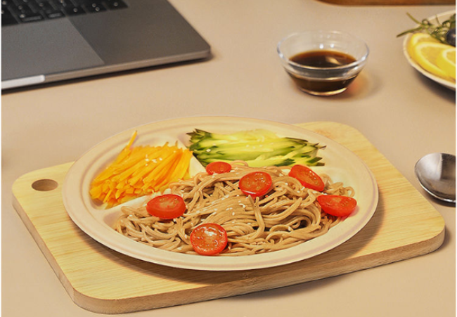 A bamboo fiber plate with noodles, cherry tomatoes, cucumber slices, and shredded carrots