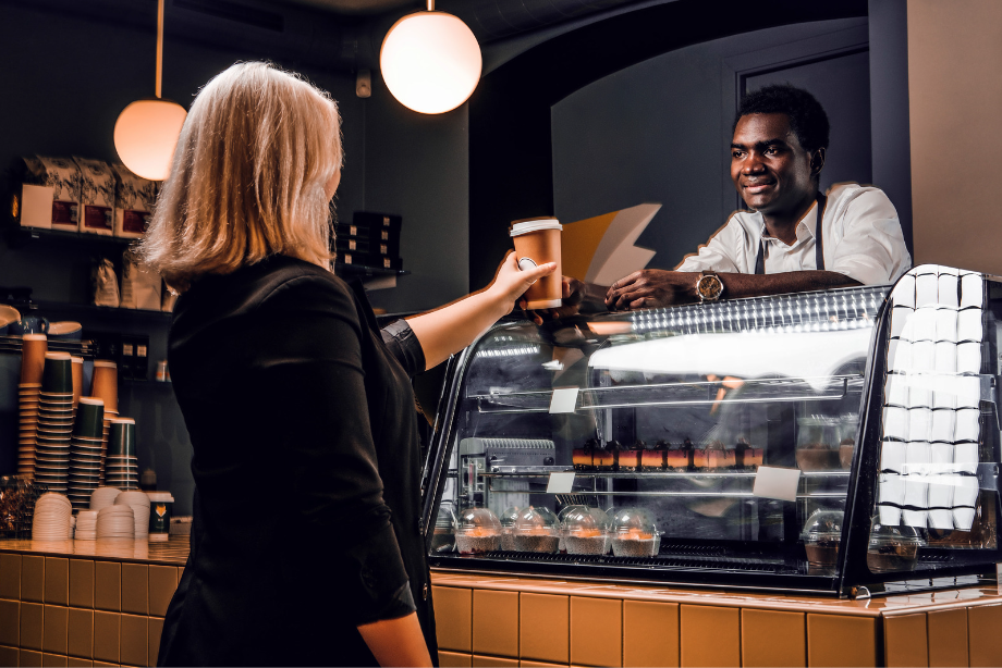 A barista handing over an eco-friendly coffee cup to a customer in a modern café, promoting sustainable coffee options.