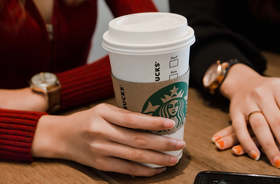 Close-up of a hand holding a coffee cup with a Starbucks logo, showcasing a sustainable paper sleeve