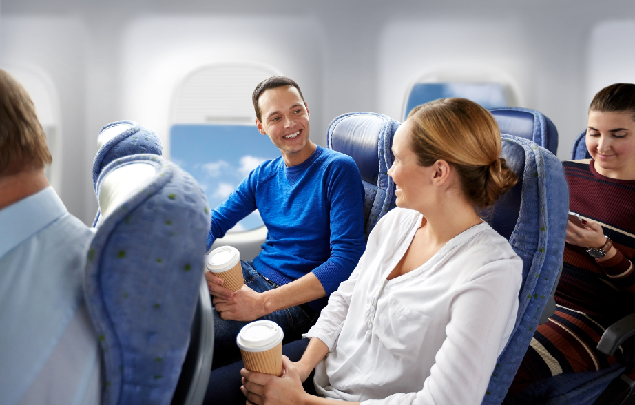 Passengers on a flight enjoying coffee in eco-friendly cups, seated together in an airplane cabin.