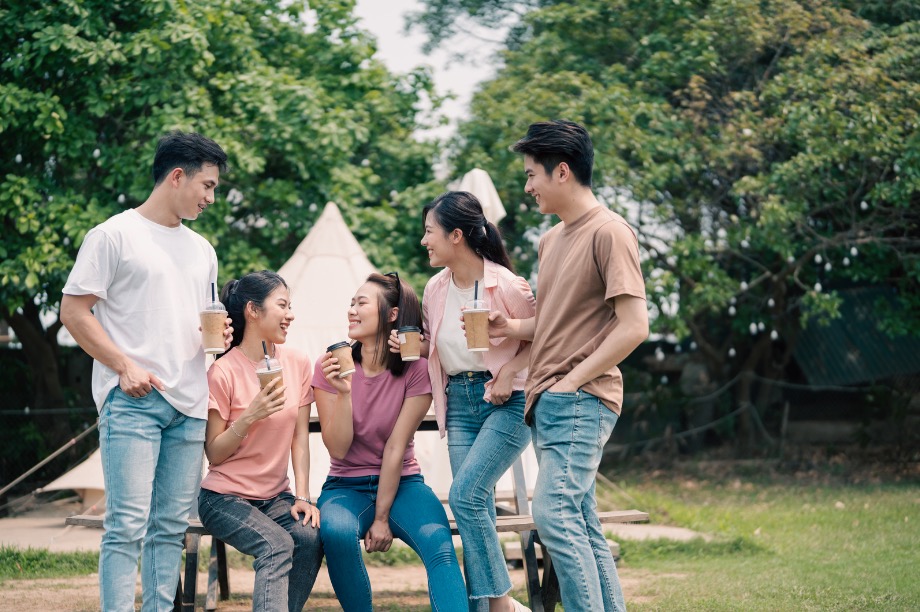 A group of five friends enjoying iced drinks outdoors, each holding a coffee cup with a sustainable lid.