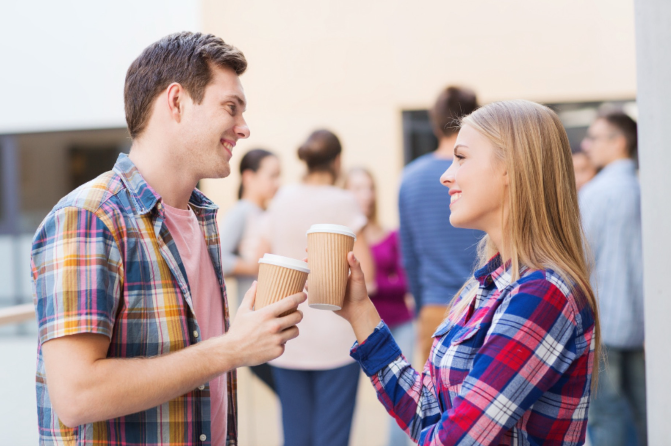 Two people smiling and clinking eco-friendly kraft paper coffee cups in a social setting, promoting sustainable coffee options.