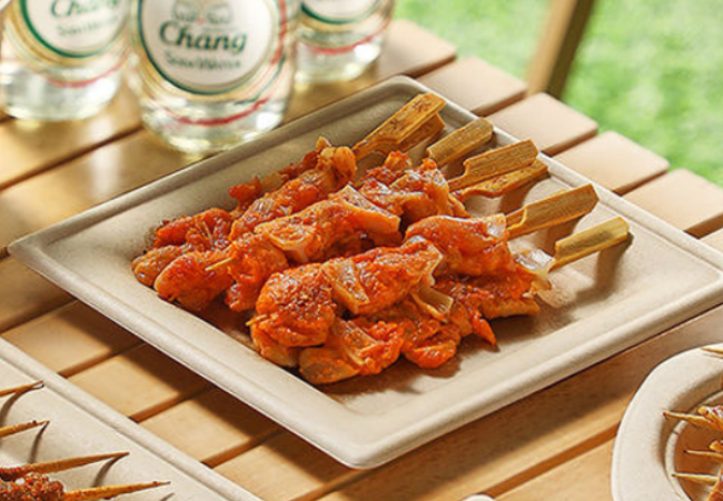 Grilled skewers served on a bamboo fiber plate, placed on an outdoor wooden table