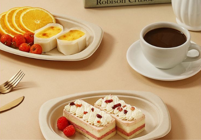 Desserts and coffee served on bamboo fiber plates, including cakes, orange slices, and custard