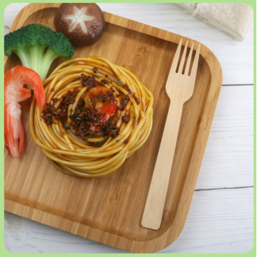 A bamboo fork placed on a bamboo plate with spaghetti, shrimp, broccoli, and a shiitake mushroom.