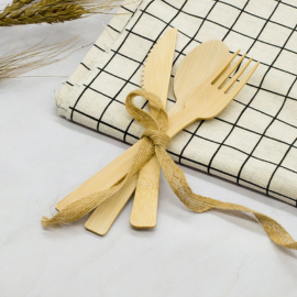 Bamboo cutlery set with spoon, fork, and knife tied with a ribbon on a checkered napkin, showcasing eco-friendly utensils.